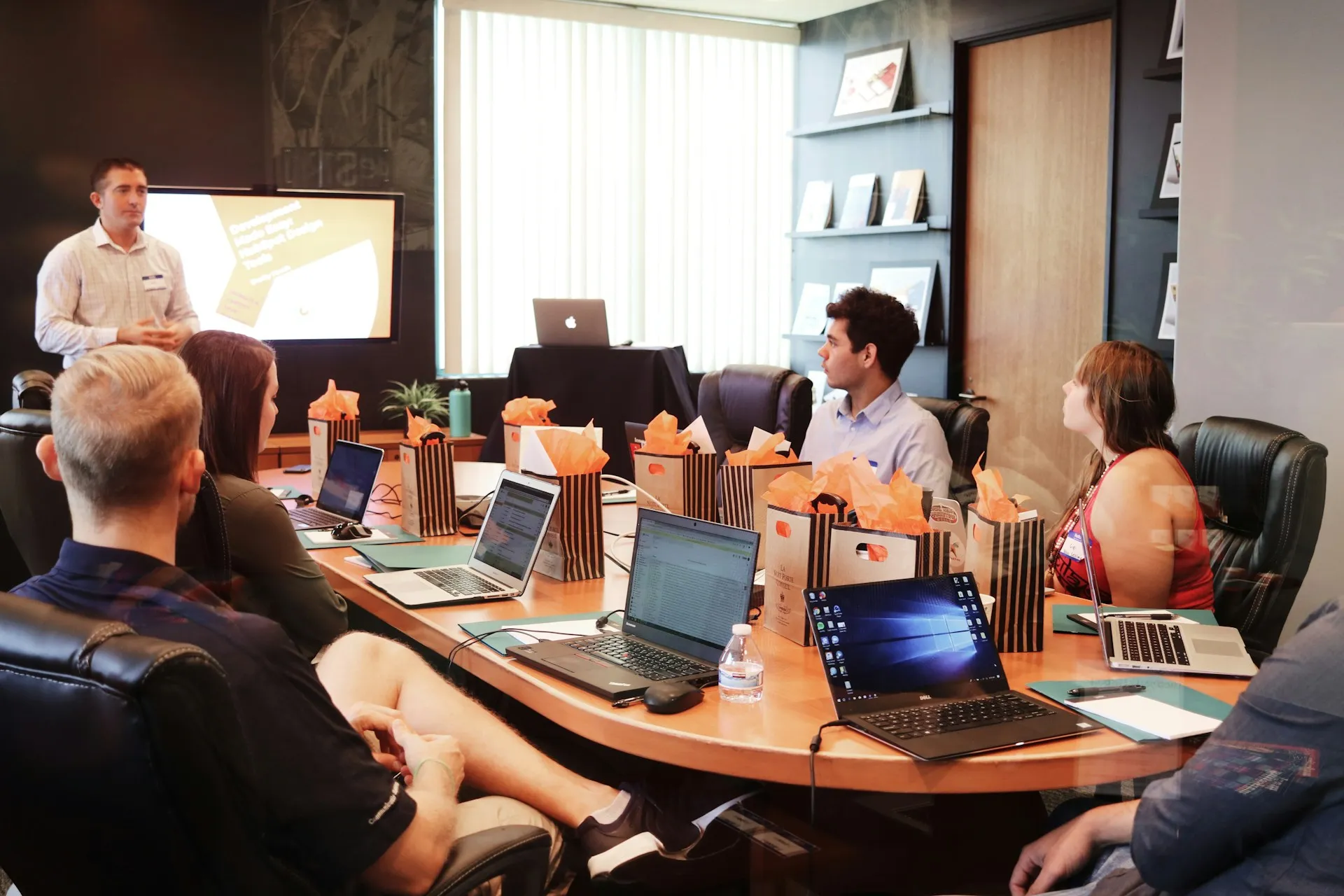 Equipo de trabajo en sala de reuniones con portátiles y presentación corporativa